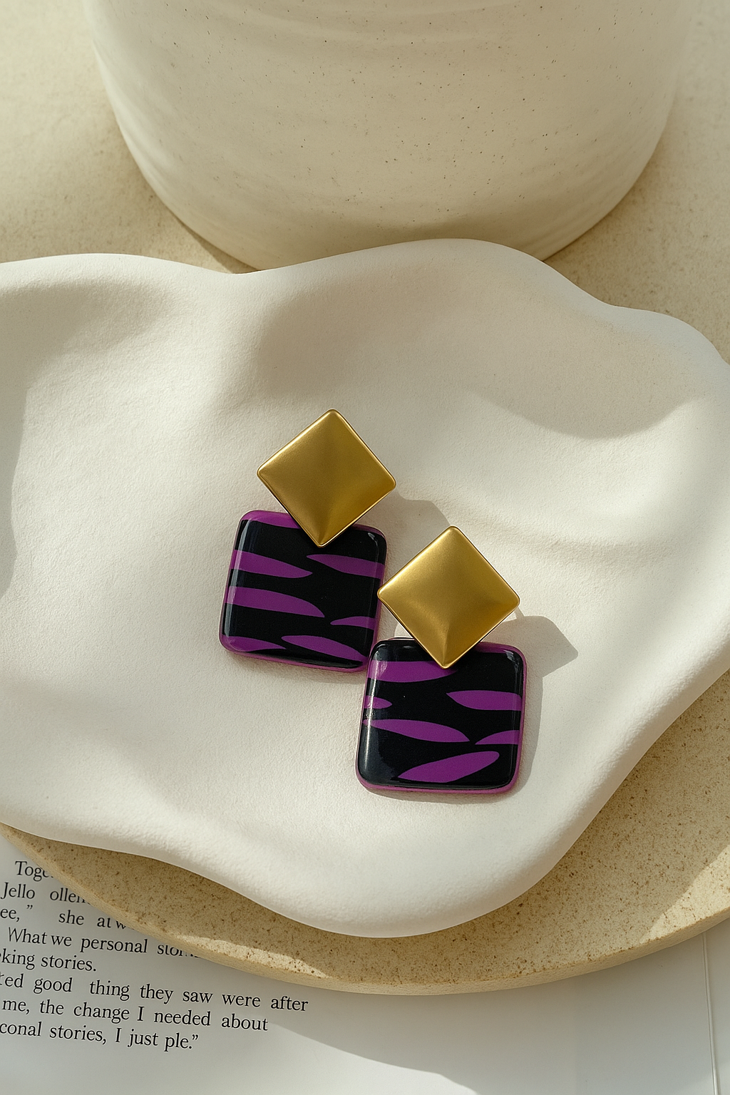 Pendientes artesanales Chorlita con diseño geométrico dorado y base cuadrada negra con rayas fucsias, fotografiados sobre fondo cerámico.